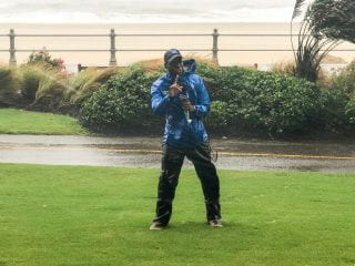 Tevin Wooten speaking on air of The Weather Channel during a storm with a beach line and ocean in the background.